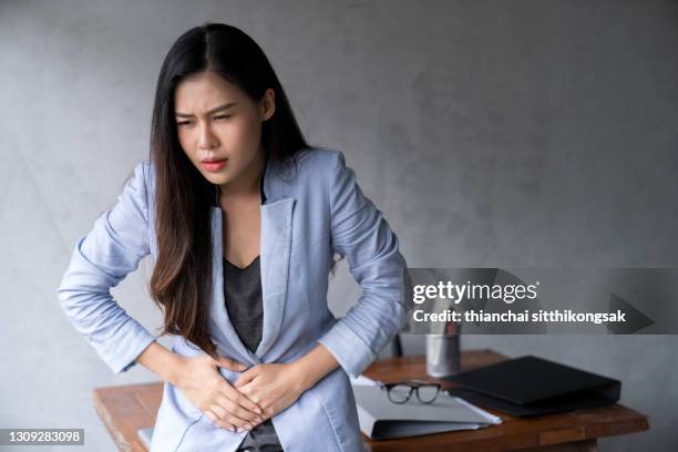 unhealthy young asian businesswoman with stomachache in office. - gastroenteritis stock pictures, royalty-free photos & images