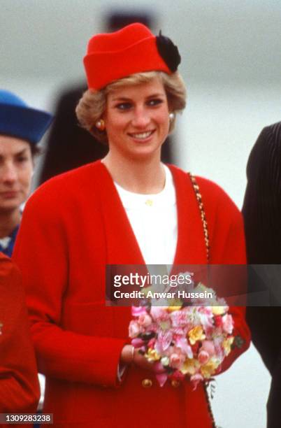 Diana, Princess of Wales, wearing a red coat with gold buttons and a matching hat designed by Chanel, smiles as she arrives at Orly Airport on...