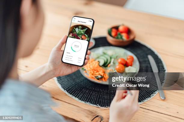 young woman using calorie counter app on smartphone while eating salad - fazer dieta imagens e fotografias de stock