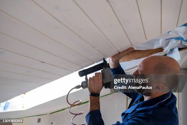 mann mit nagelpistole für dachpaneele hausrenovierung - deckenverkleidung holz stock-fotos und bilder