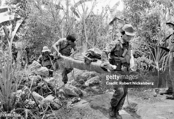 View of Salvadoran Army soldiers as they carry a body bag on a stretcher, Tejutepeque, El Salvador, March 26, 1984. They'd been involved in a battle...