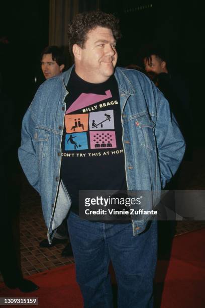 American actor and comedian George Wendt wearing a denim jacket over a black t-shirt with the cover of the Billy Bragg album 'Don't Try This at Home'...