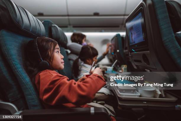 lovely little girl watching movie on the seat-back tv screen while enjoying her airline meal - airplane stock pictures, royalty-free photos & images