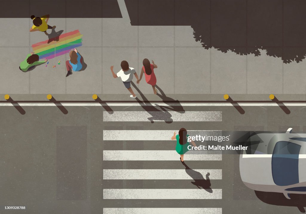 View from above pedestrians crossing street by kids coloring rainbow on sidewalk