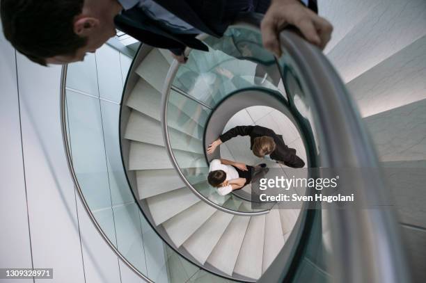 businessman watching colleagues talk at bottom of spiral staircase - witness bildbanksfoton och bilder