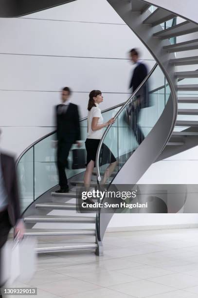 young businesswoman ascending spiral staircase in office - spiral staircase stockfoto's en -beelden
