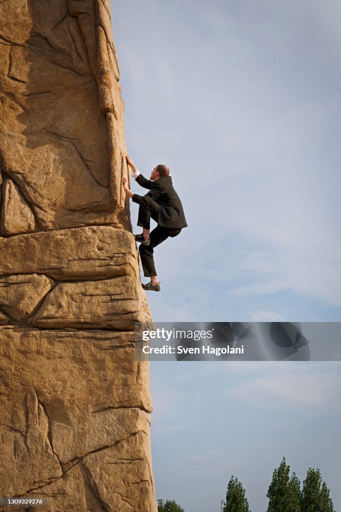 Businessman climbing steep rock face