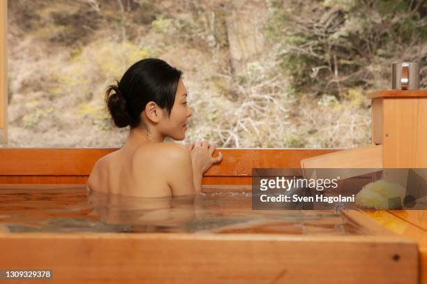 young woman soaking in onsen tub - sven hagolani stock-fotos und bilder