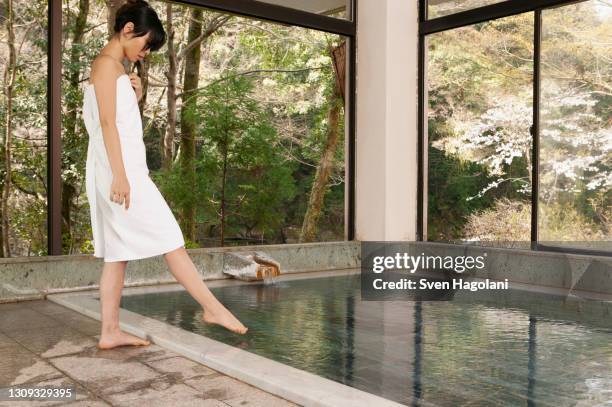 young woman in towel dipping toe in water at onsen - sven hagolani stock-fotos und bilder