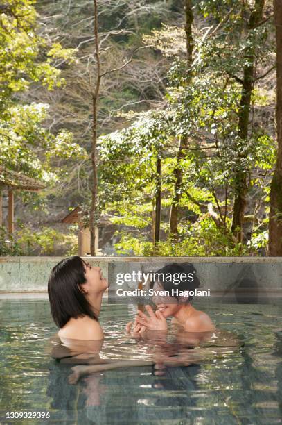 happy young women friends soaking in pool at onsen - sven hagolani stock pictures, royalty-free photos & images