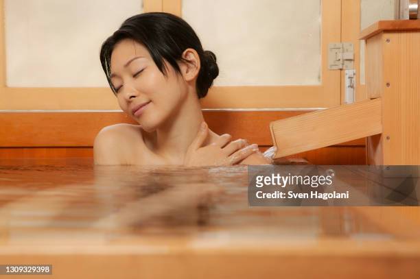 serene young woman enjoying soak in pool at onsen - sven hagolani stock-fotos und bilder