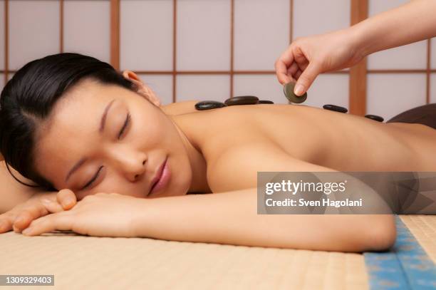 tranquil young woman receiving hot stone massage at spa - sven hagolani stock-fotos und bilder
