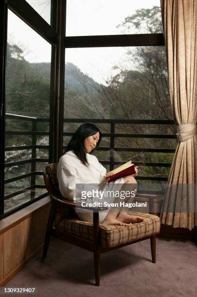 young woman in bathrobe reading book in window corner - sven hagolani stock pictures, royalty-free photos & images