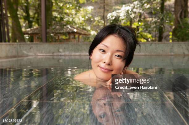 portrait beautiful young woman soaking in pool at tranquil onsen - sven hagolani stock pictures, royalty-free photos & images