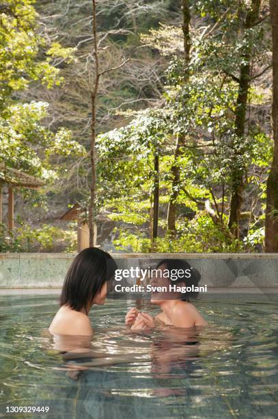 happy young women friends laughing in soaking pool at onsen - sven hagolani stock-fotos und bilder