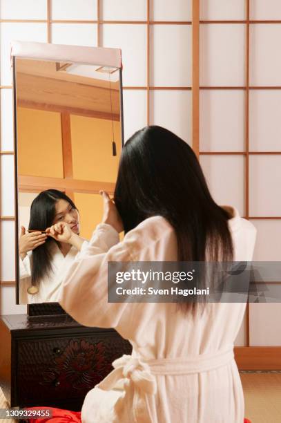 young woman in bathrobe combing hair at mirror in spa - sven hagolani stock-fotos und bilder