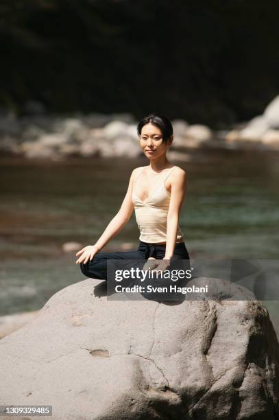 portrait beautiful young woman meditating in lotus pose on sunny rock - sven hagolani stock-fotos und bilder