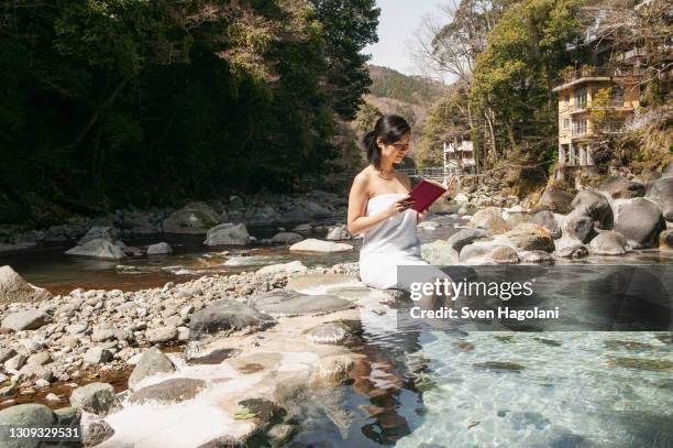 young woman in towel reading book at sunny pool at onsen, izu, japan - sven hagolani stock-fotos und bilder