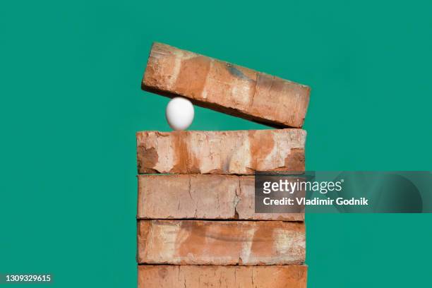 egg between bricks on green background - vulnerability stock pictures, royalty-free photos & images