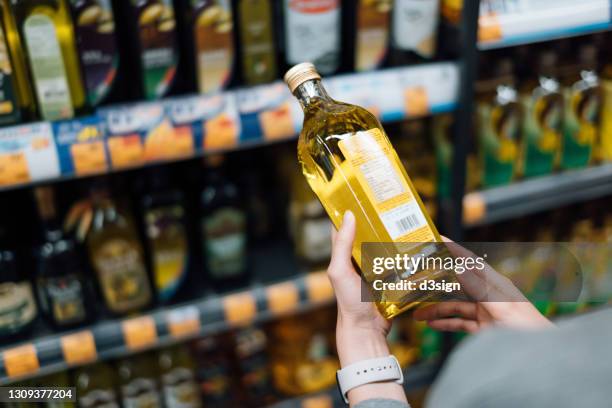 close up of young woman grocery shopping in a supermarket. standing by the aisle, holding a bottle of organic cooking oil, reading the nutritional label and checking ingredients at the back - grasso nutrienti foto e immagini stock