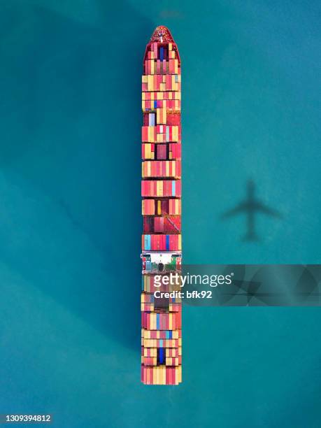 airplane flying over container ship in the ocean. - container ship stock pictures, royalty-free photos & images