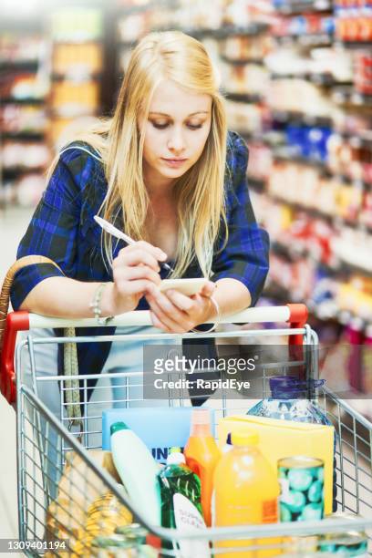 beautiful young blonde woman concentrates on checking her shopping list in a supermarket - plentiful imagens e fotografias de stock
