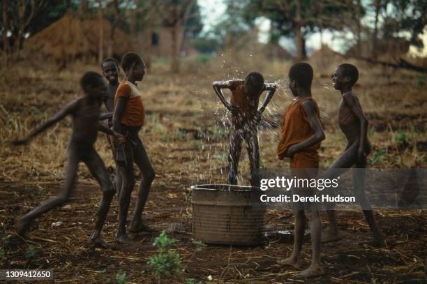 Sudanese refugee boys pictured laughing while one boy splashes himself with water at an abandoned mission near Palotaka, South Sudan, two hundred...