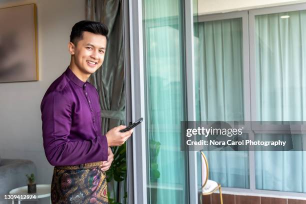 malaysian man with malay attire holding a smart phone - handsome muslim men stock pictures, royalty-free photos & images