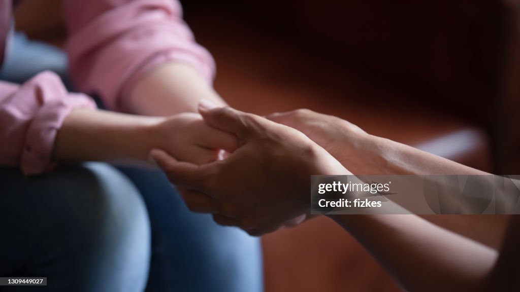 Biracial female psychologist hands holding palms of millennial woman patient