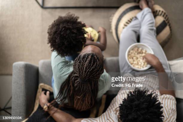 vista ad alto angolo della famiglia che mangia popcorn e guarda la tv a casa - african family eating foto e immagini stock