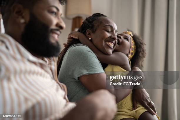 süßes mädchen, das mutter zu hause umarmt - african family stock-fotos und bilder