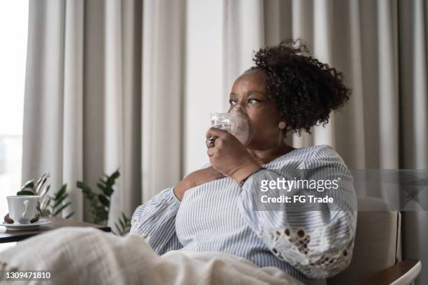mujer madura usando una máscara de inhalación en casa - nebulizador fotografías e imágenes de stock