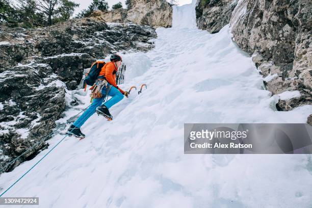 ice climber stands on front points of crampons while climbing frozen waterfall - crampon stock pictures, royalty-free photos & images