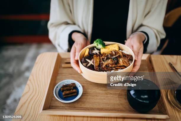 close up mid-section of young asian woman enjoying japanese style grilled pork with vegetables and rice freshly served in a traditional wooden lunch box, with miso soup by the side in restaurant. eating out lifestyle, healthy eating with comfort food - bento imagens e fotografias de stock