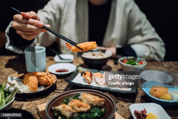 close up mid-section of young asian woman enjoying delicate japanese style cuisine with assorted sushi, seafood tempura and grilled oysters freshly served on the dining table in a restaurant. asian cuisine and food. eating out lifestyle - tempura stock-fotos und bilder