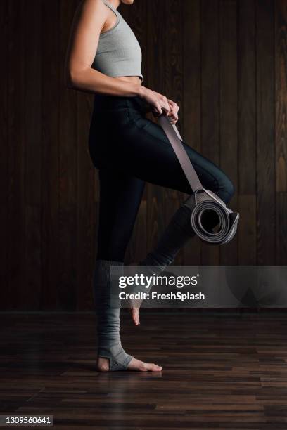 side view of an unrecognizable female athlete standing in front of a dark wooden wall (vertical) - knee stock pictures, royalty-free photos & images
