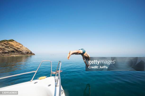 young adult man diving from his yacht - jumping sun stock pictures, royalty-free photos & images