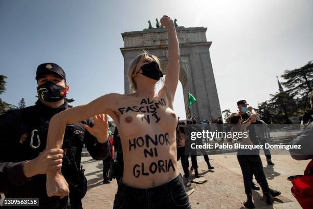 Activist with body paint reading 'To fascism neither honor, nor glory.' raises her fist as she is lead away by police during a gathering of...