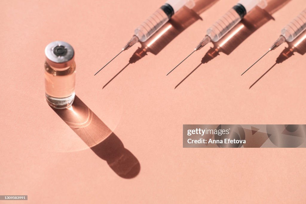 Pattern made with many plastic disposable sterile syringe and sealed vial of liquid remedy placed on pastel peach orange background with shadows and light reflections. Flat lay style