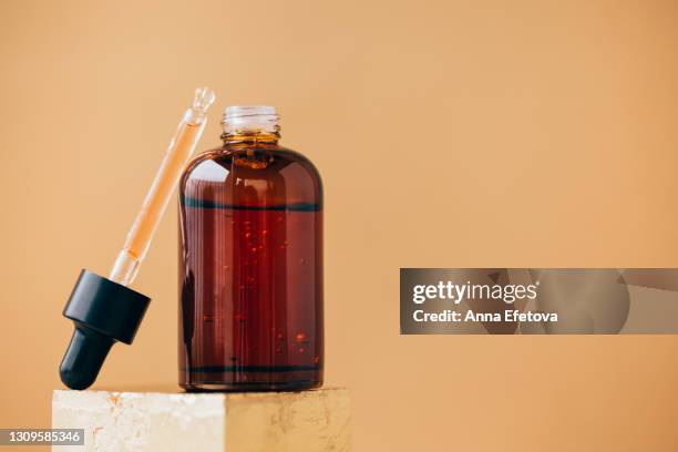 amber glass bottle with essential oil and many air bubbles placed on gold podium near pipette on beige background. concept of natural cosmetic products. front view and extreme close-up - vitamin c stock pictures, royalty-free photos & images