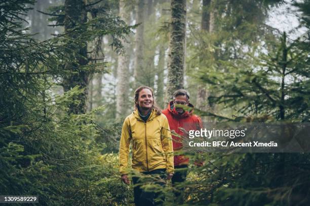 mature couple hike through forest on a rainy day - dreiviertelansicht stock-fotos und bilder