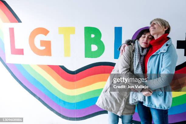 a lesbian couple embraces with eyes closed in front of a pride flag graffiti. - the love parade stock pictures, royalty-free photos & images