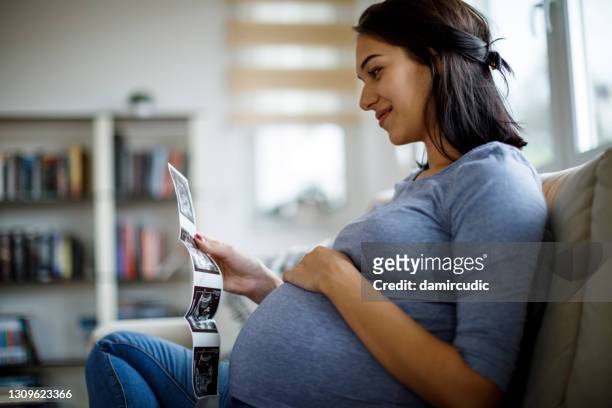 happy pregnant woman looking at ultrasound scan at home - prenatal care stock pictures, royalty-free photos & images