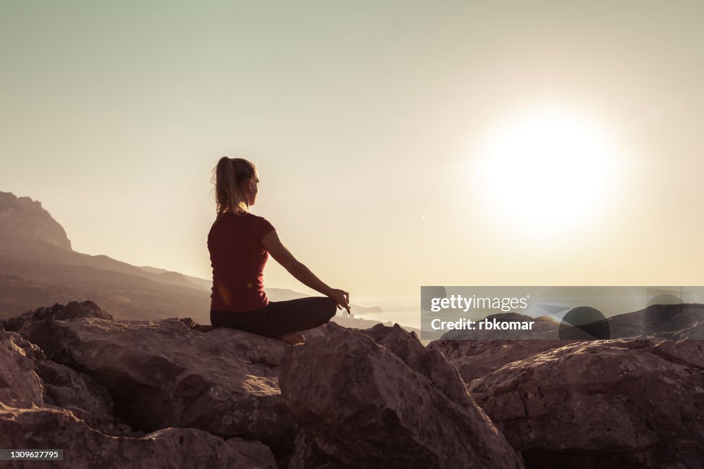 Young woman practices yoga and meditates on the mountain