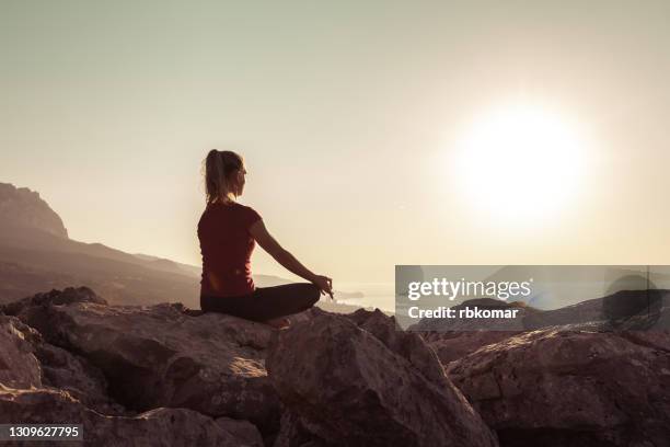 young woman practices yoga and meditates on the mountain - lotuspositie stockfoto's en -beelden