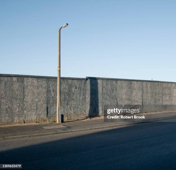 wooden fence, lamp post, road in shadow. industrial area of sandwell, west midlands. - entsättigt stock-fotos und bilder