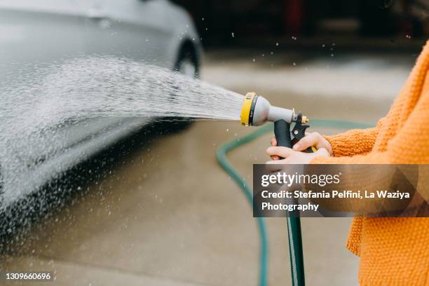 little girl's hands holding a hose spraying hose while washing a car - wet hose ストックフォトと画像