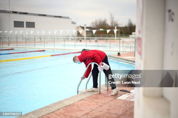 An attendant sanitises the hand rails as swimmers take to the 14 degree water in the open-air lido at Hillingdon leisure centre on March 29, 2021 in...