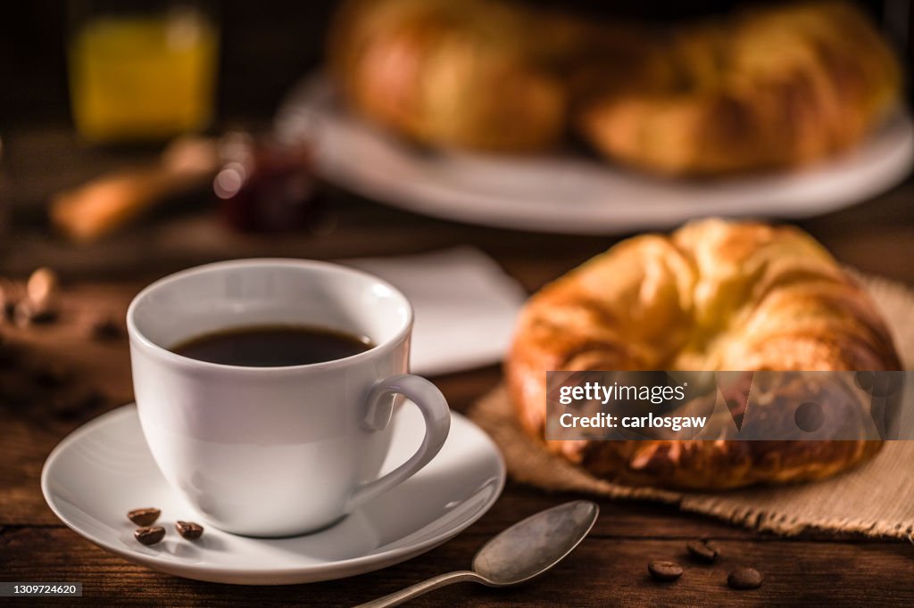 Coffee cup and fresh French croissant on a rustic wooden table