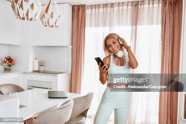 schöne blonde weibliche lächeln beim hören von musik auf dem smartphone - fernseher tanzen home stock-fotos und bilder